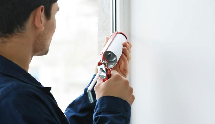 A close-up of a technician expertly applying white sealant to a window joint with a caulking gun.