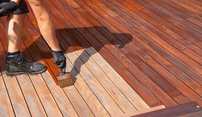 A professional applying wood stain to a deck surface, enhancing color while ensuring even coverage and long-lasting protection