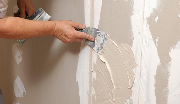 Skilled worker repairing interior drywall, ensuring even surface and seamless finish