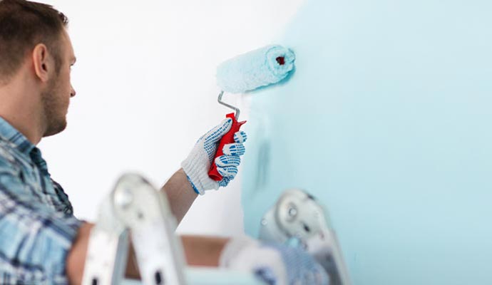 A painter using a roller to apply light blue eggshell paint on a wall