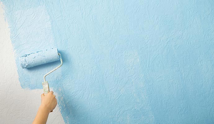 Painter coating a wall with light blue emulsion paint using a roller
