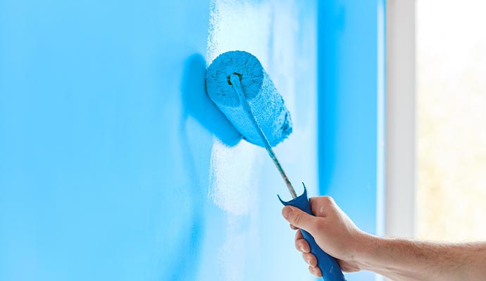 A painter using a roller to apply paint evenly on a wall