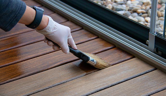a painter applying fresh coat of stain on deck