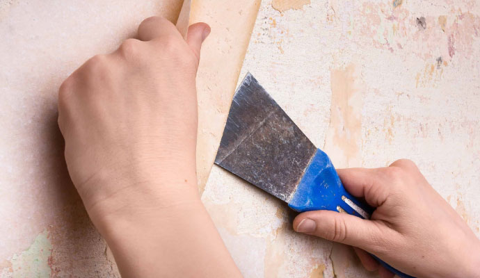 Person removing old wallpaper from wall